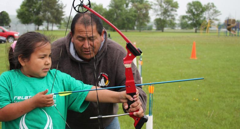 A 4-H volunteer helps a 4-H kid practice archery