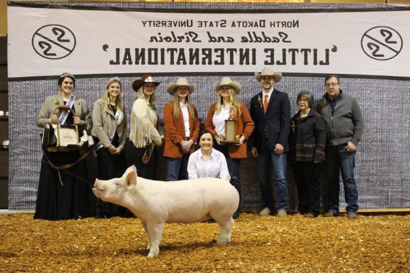 members pose behind a pig in an arena with a banner in the background